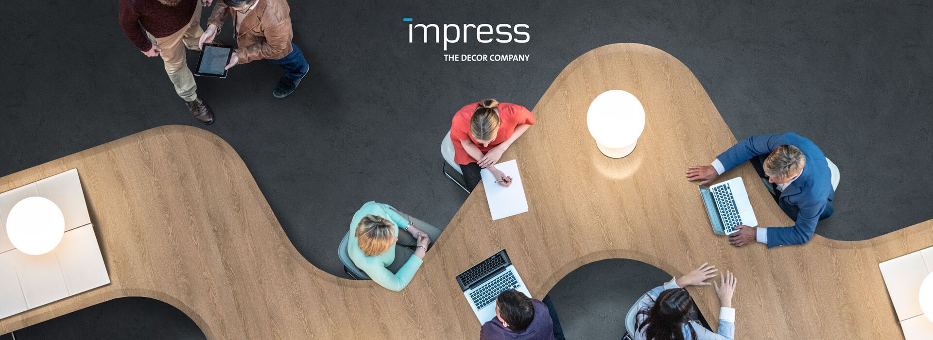 Logo of impress on a picture of a long modern desk and working team members.